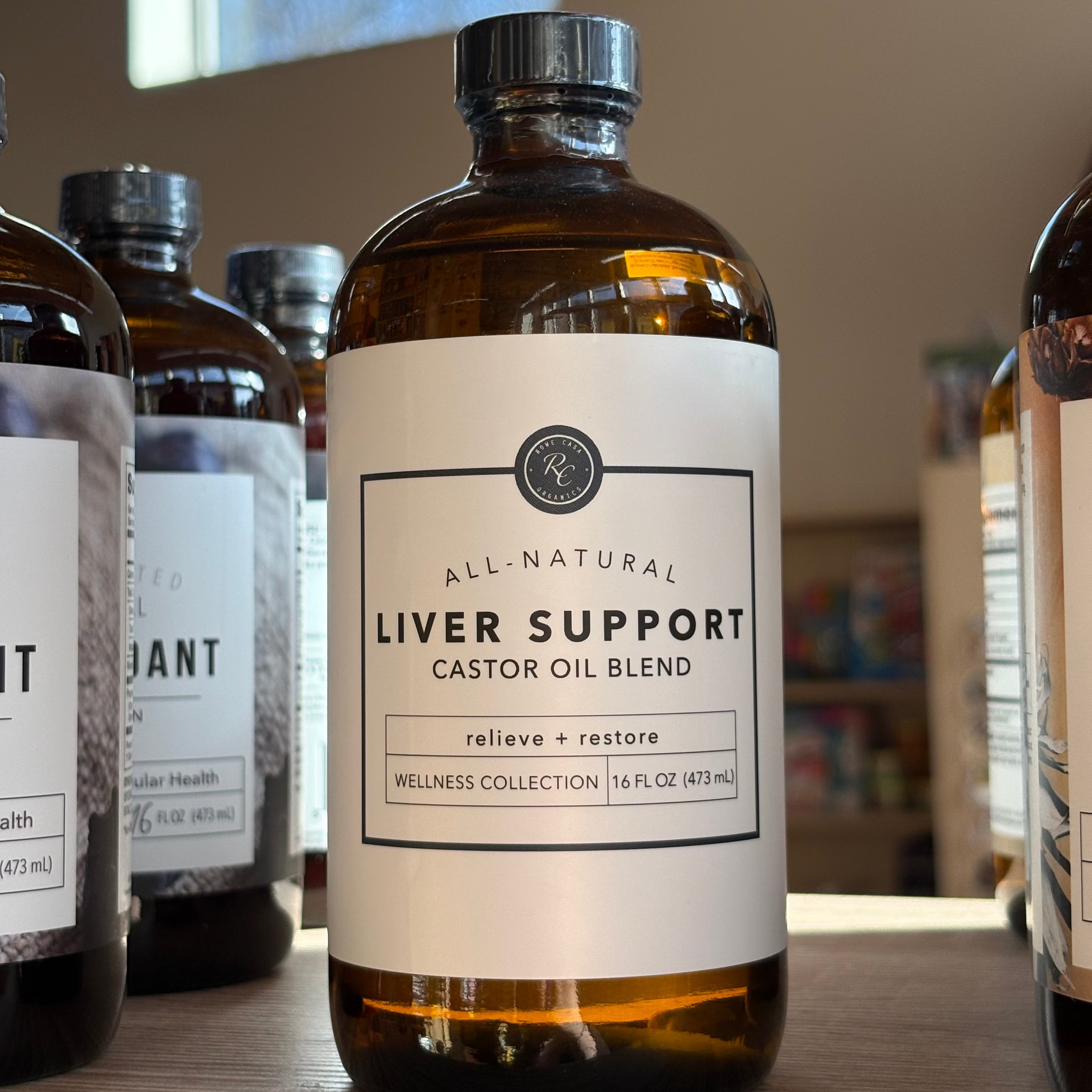 Bottle of 'All-Natural Liver Support' castor oil blend on a wooden surface with other similar bottles in the background.