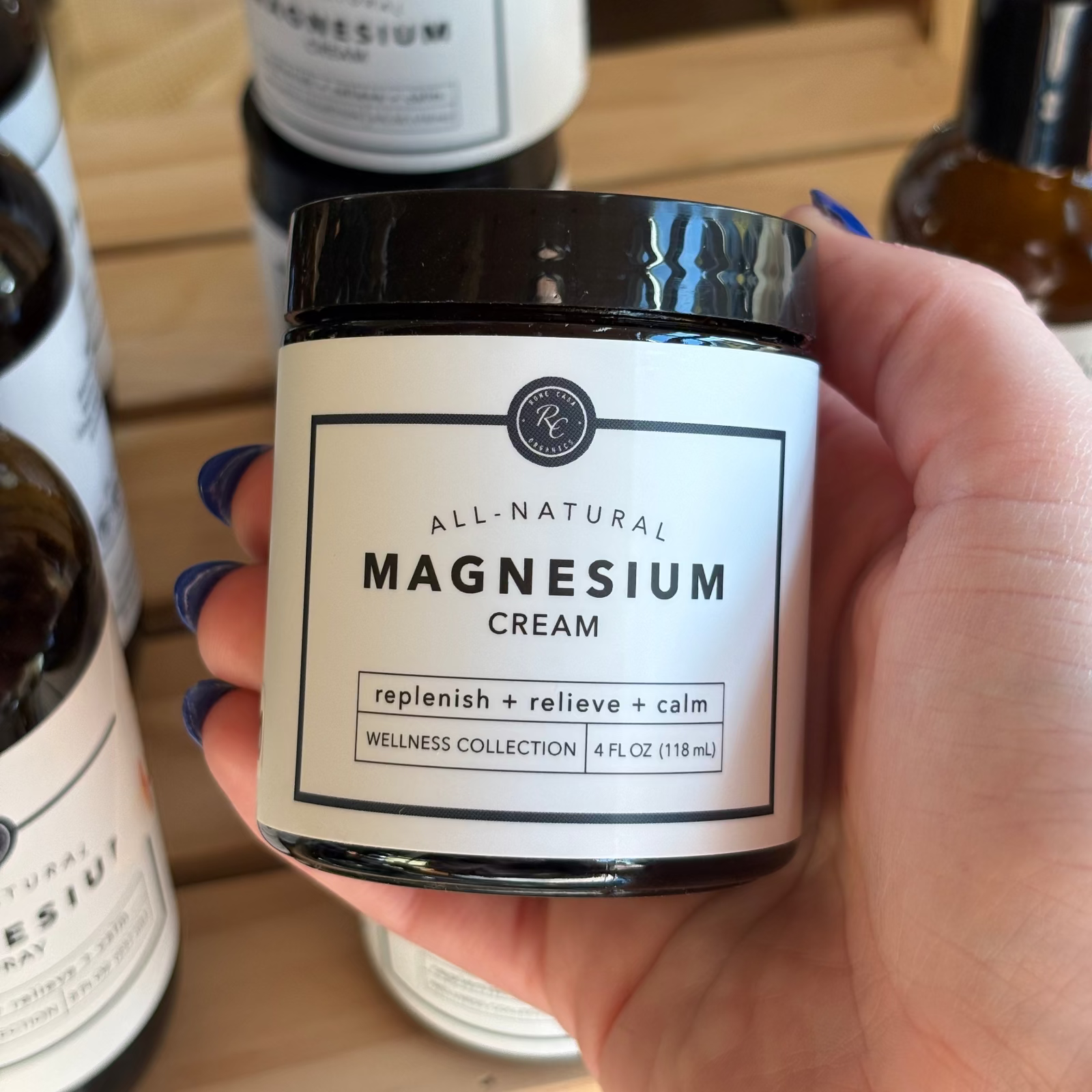 Hand holding a jar of Rowe Casa all-natural magnesium cream with a label on a wooden surface.
