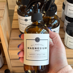 Hand holding an Rowe Casa all-natural magnesium spray bottle with a blurred store background