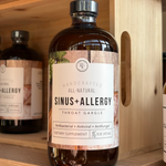 Bottle of Rowe Casa 'Sinus + Allergy' throat gargle on a wooden shelf with other similar products.