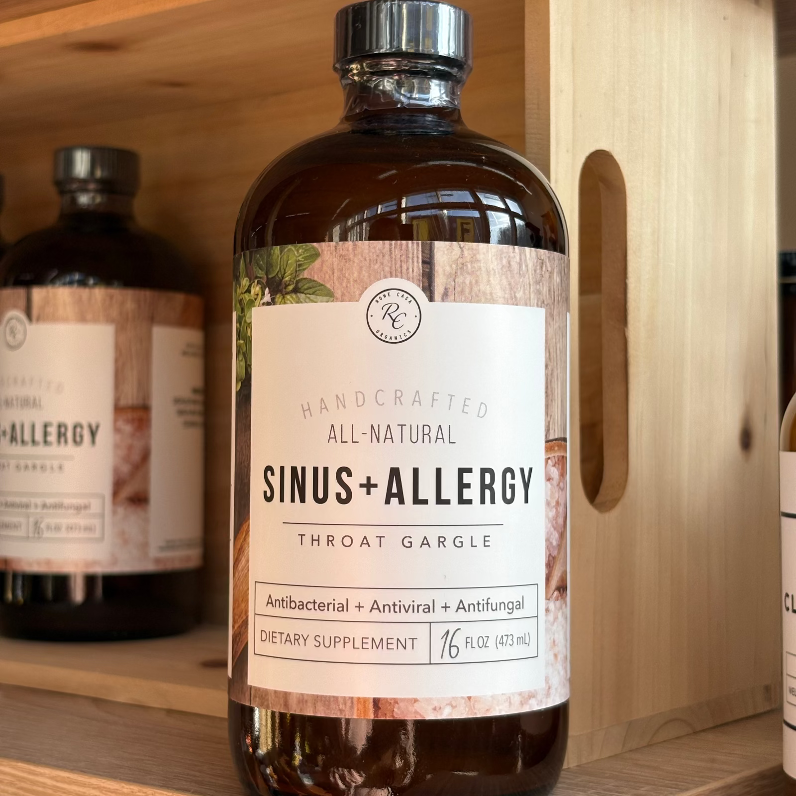 Bottle of Rowe Casa 'Sinus + Allergy' throat gargle on a wooden shelf with other similar products.