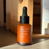 Orange serum bottle with black dropper labeled 'Rowe Casa Organics' on a wooden surface.