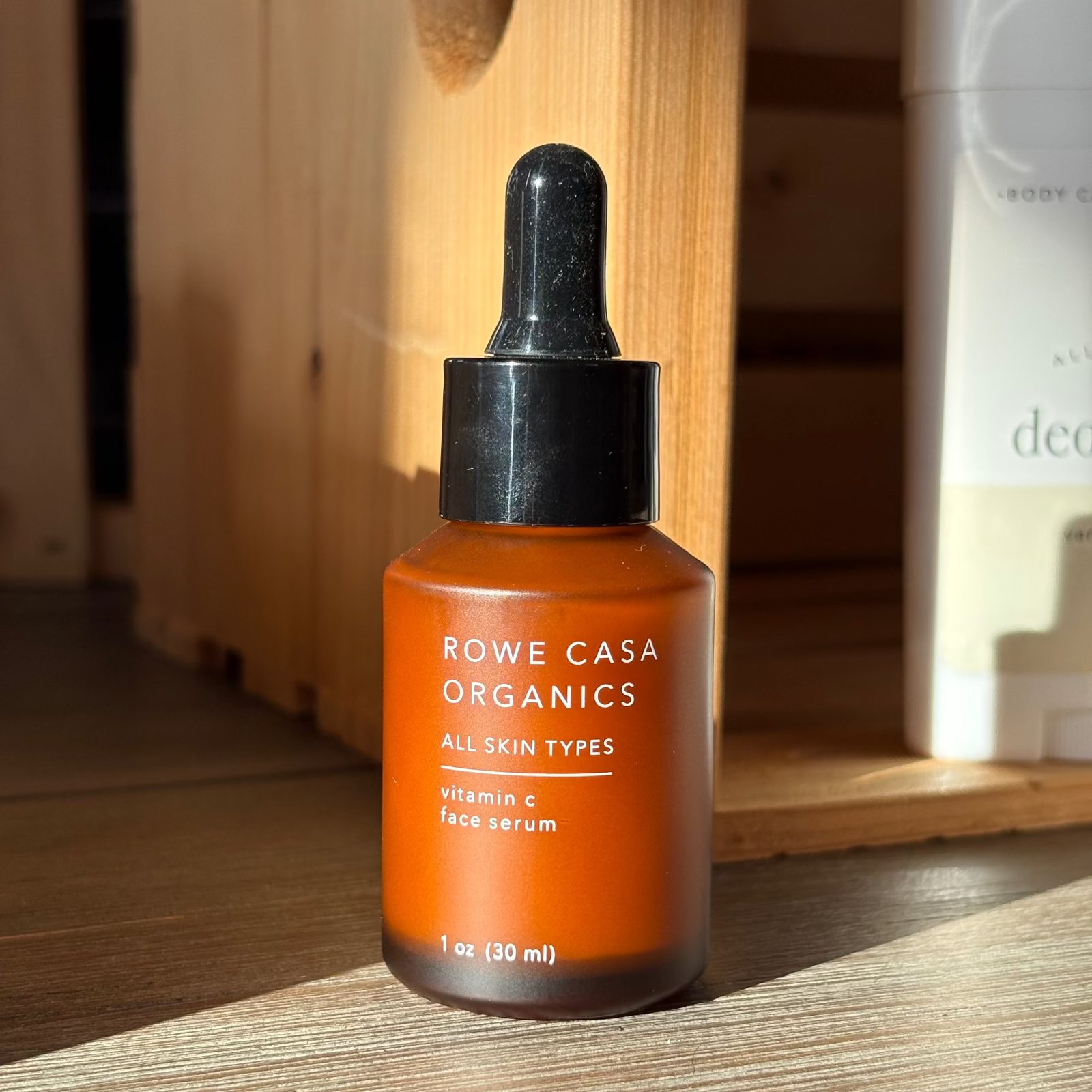 Orange serum bottle with black dropper labeled 'Rowe Casa Organics' on a wooden surface.