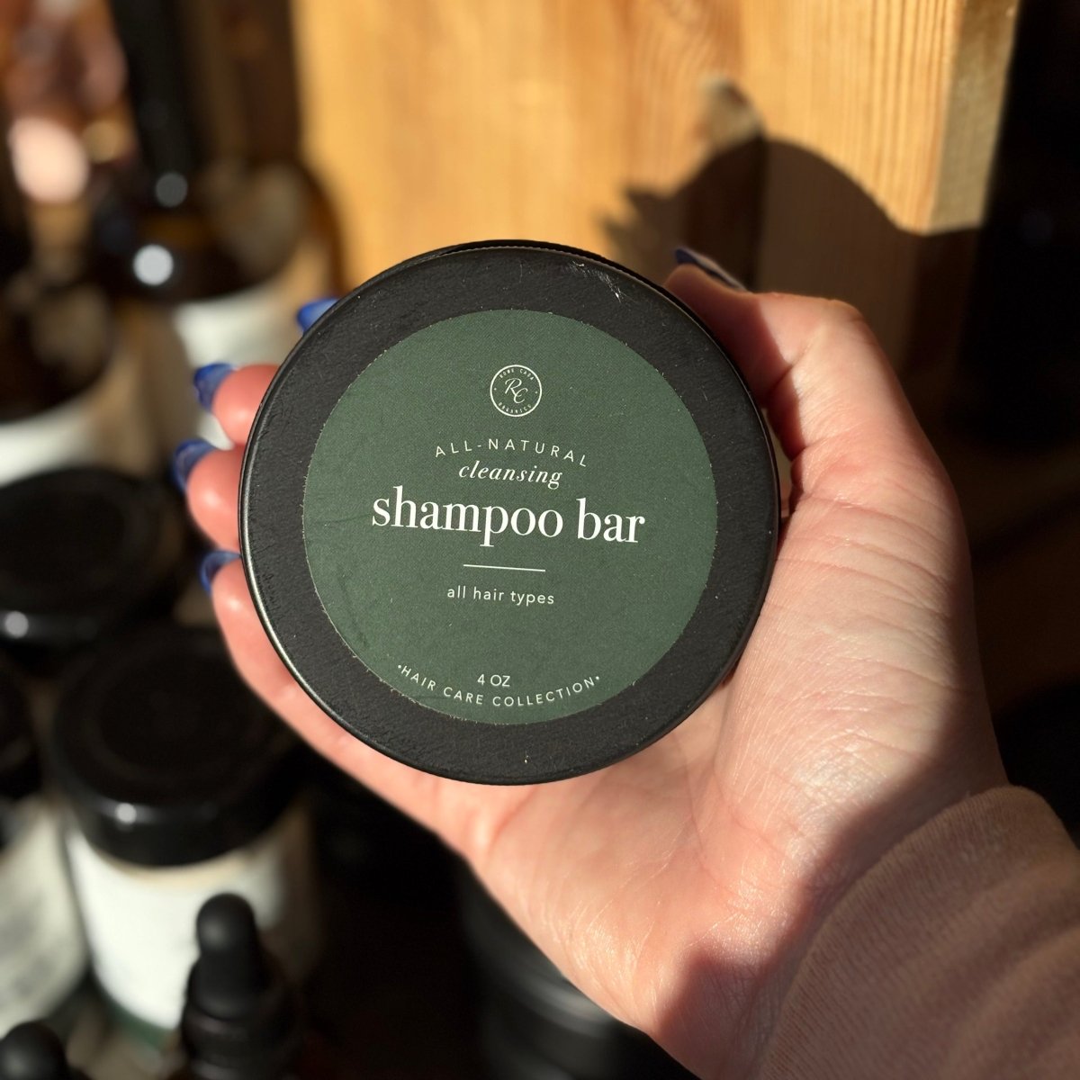 Hand holding a container labeled 'shampoo bar' with a blurred background of bottles.