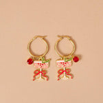 Gold hoop earrings with wine glass and bow designs on a beige background