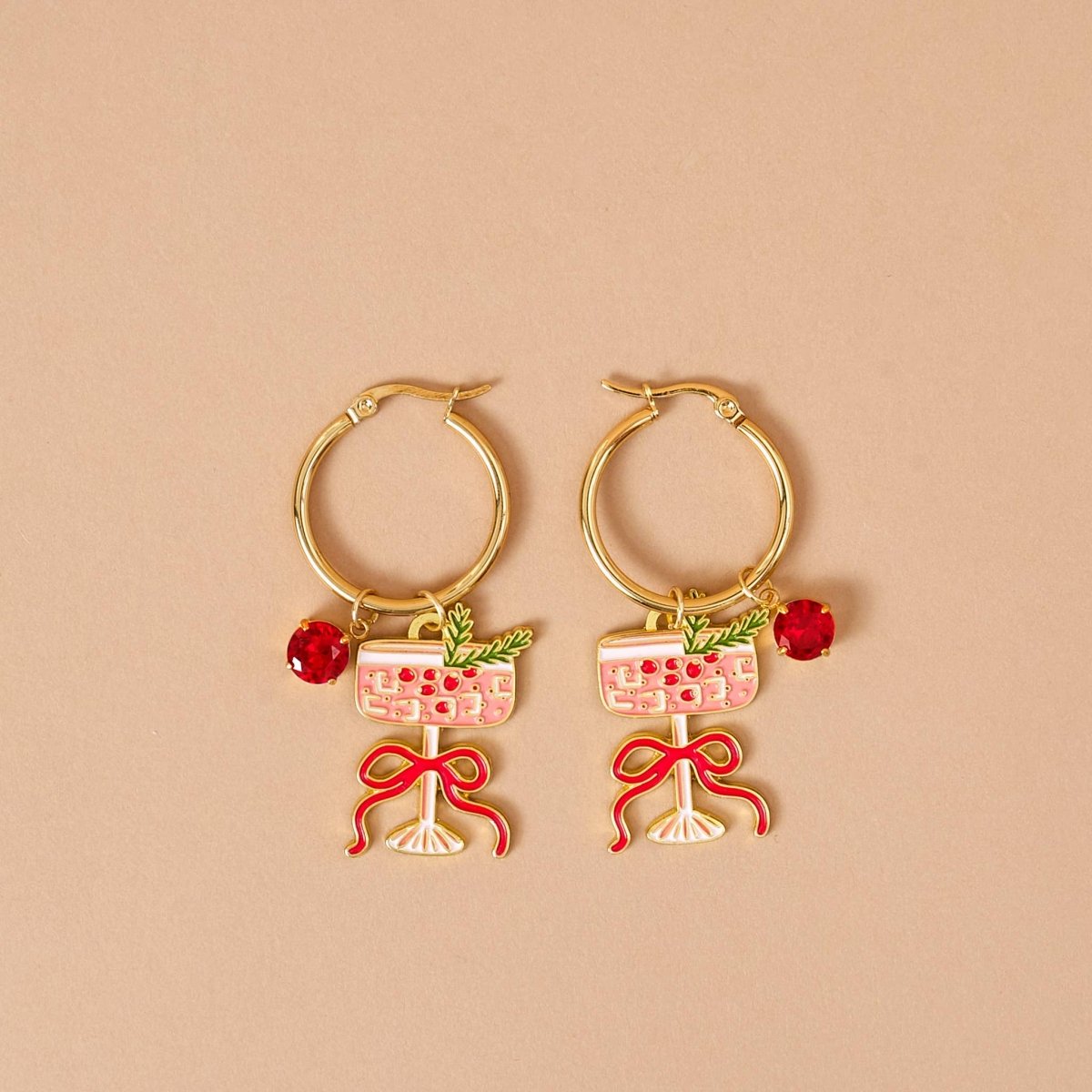 Gold hoop earrings with wine glass and bow designs on a beige background