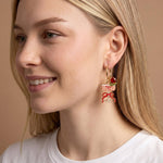 Close-up of a woman wearing a unique earring with a decorative design on a beige background