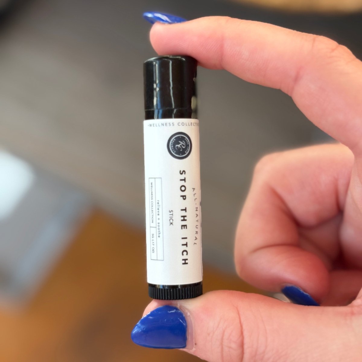 Hand holding a small tube labeled 'Stop The Itch' with a blurred background.