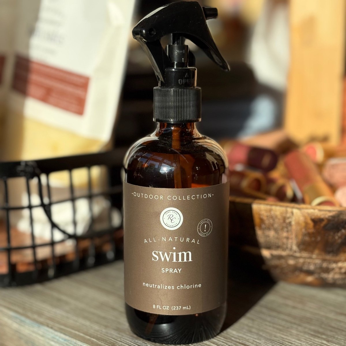 Brown spray bottle labeled 'All Natural Swim Spray' on a wooden surface with a blurred background.