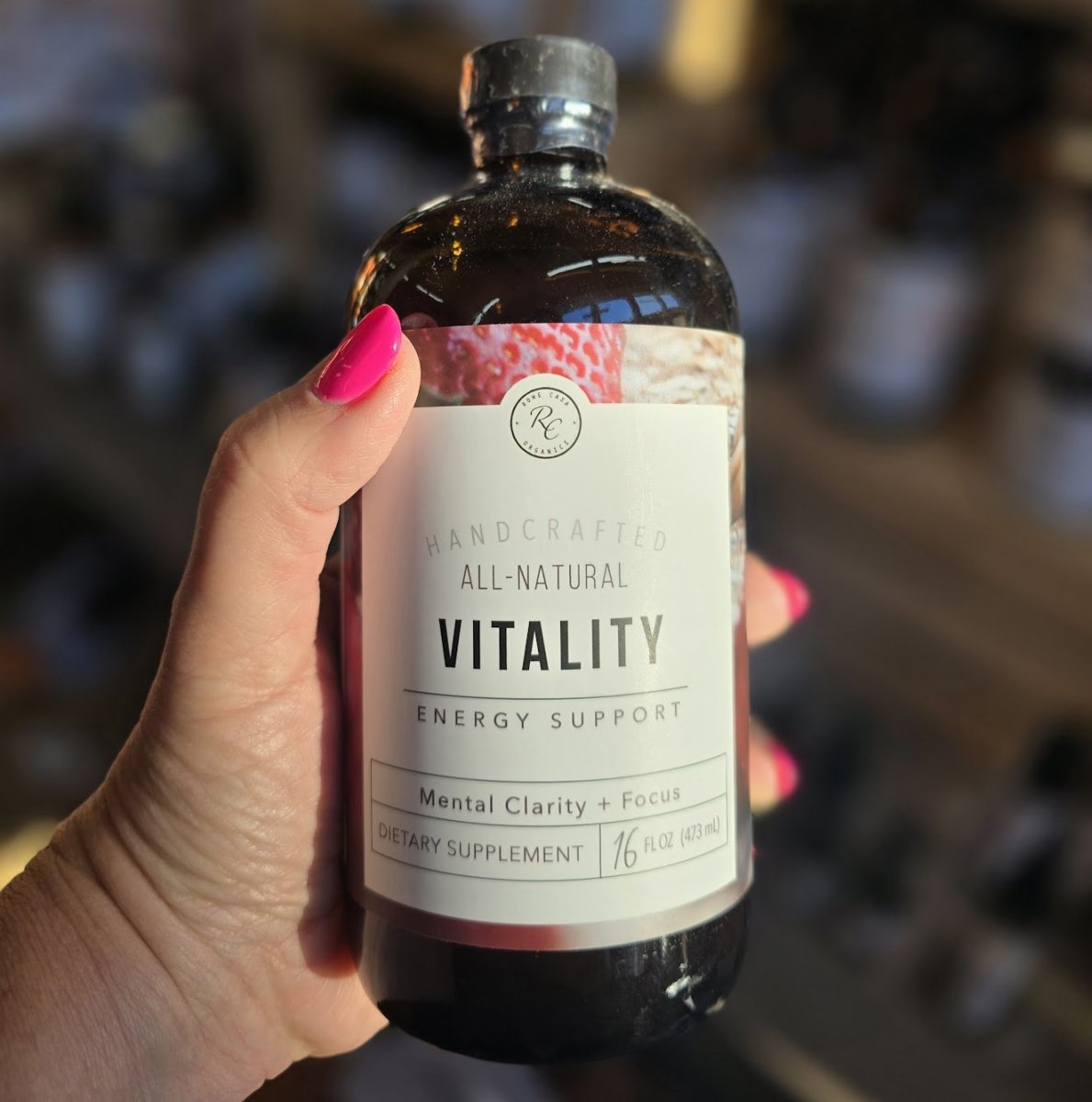 Bottle of 'Vitality' energy support supplement held by a hand with pink nail polish.