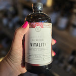 Bottle of 'Vitality' energy support supplement held by a hand with pink nail polish.