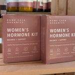 Two boxes of Rowe Casa Organics Women's Hormone Kit on a wooden surface with bottles in the background.